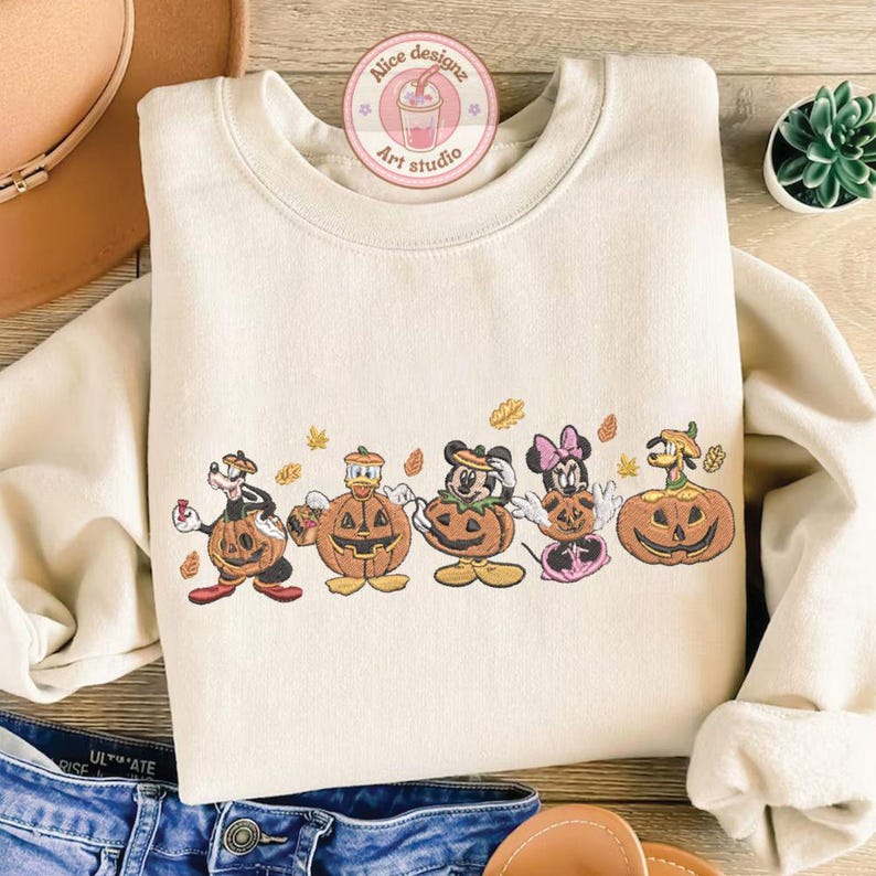 Puede incluir: Sudadera de color crema con un dise&ntilde;o bordado de personajes de dibujos animados disfrazados de calabazas. El dise&ntilde;o incluye un perro, un pato, Mickey Mouse, Minnie Mouse y un personaje con cabeza de calabaza. La sudadera tiene cuello redondo y mangas largas.