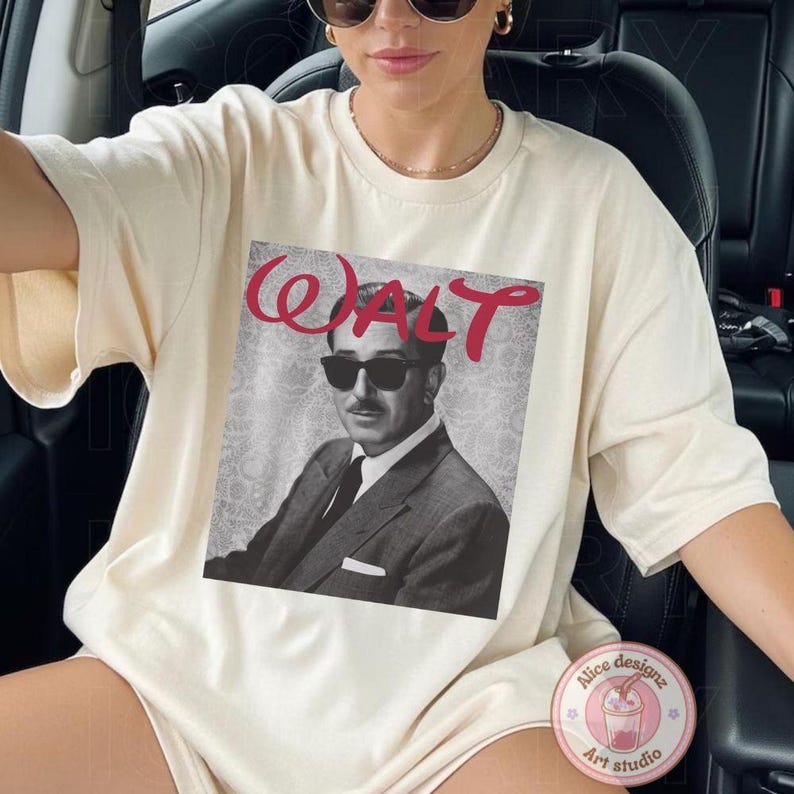 Op de afbeelding: Cr&egrave;mekleurig T-shirt met een zwart-wit afbeelding van een man met een zonnebril, met de naam "WALT" in rode letters erboven. Het shirt heeft korte mouwen en een ronde hals.