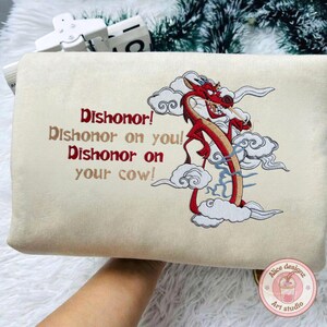 May include: Beige rectangular pouch with an embroidered red dragon design and the text "Dishonor! Dishonor on you! Dishonor on your cow!" The dragon is surrounded by white clouds. A small logo is in the bottom right corner.