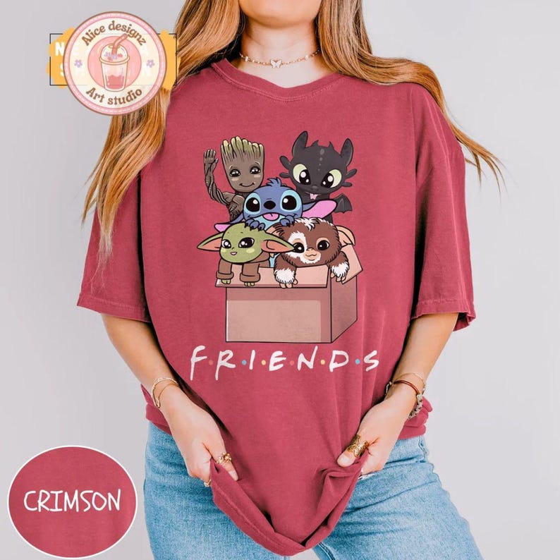 Peut inclure: T-shirt de couleur cramoisie avec un motif de personnages de dessins anim&eacute;s dans une bo&icirc;te et le mot "FRIENDS" en dessous. Le t-shirt a une coupe ample et des manches courtes. Le motif comprend des personnages comme Groot, Stitch et Krokmou.
