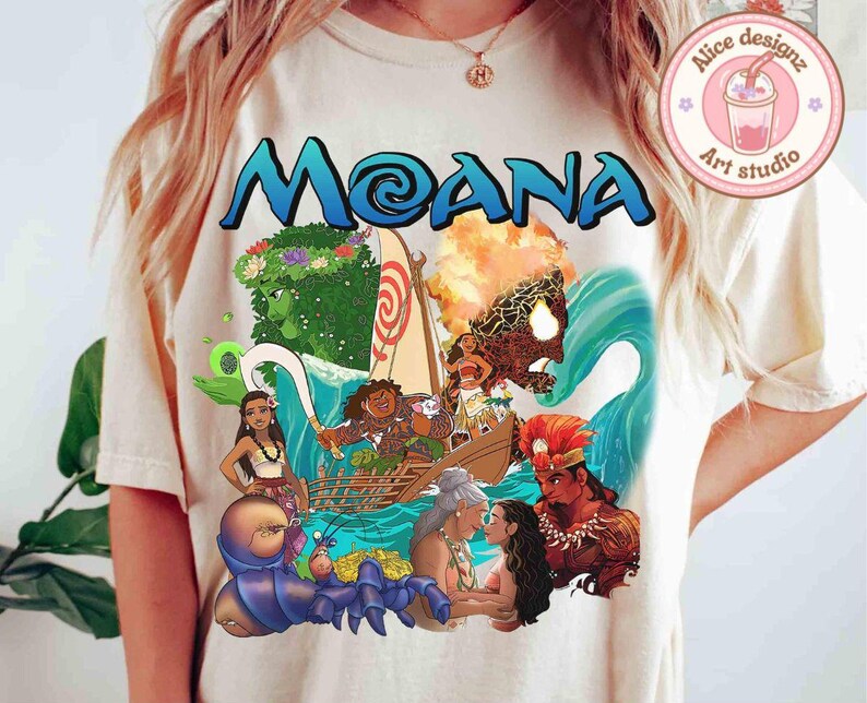 Puede incluir: Una camiseta blanca con un estampado gr&aacute;fico colorido de personajes de la pel&iacute;cula de Disney Moana. El gr&aacute;fico incluye a Moana, Maui, el semidi&oacute;s, y el oc&eacute;ano.
