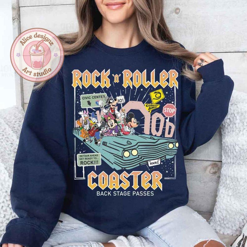 May include: A navy blue sweatshirt with a graphic print of a vintage-style cartoon roller coaster with Mickey Mouse and other Disney characters. The text "Rock 'n' Roller Coaster" is printed in yellow and red letters. The text "Back Stage Passes" is printed in white letters.