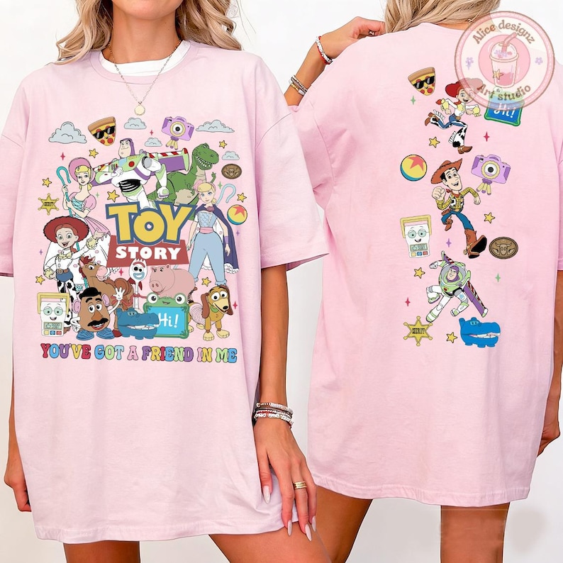 May include: A light pink t-shirt featuring a large graphic print of Toy Story characters on the front and a vertical arrangement of the same characters on the back. The front includes the text Toy Story and You've Got A Friend In Me.