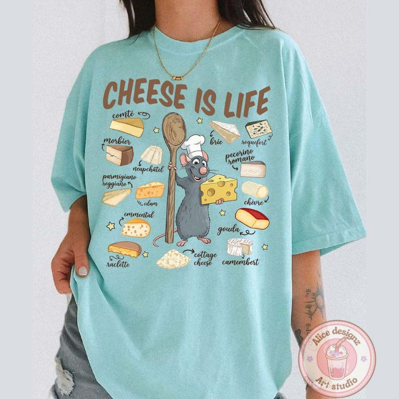Puede incluir: Camiseta azul claro con la frase "CHEESE IS LIFE" e ilustraciones de varios quesos. Un chef de dibujos animados con forma de rata sostiene una cuchara de madera y una cu&ntilde;a de queso. La camiseta tambi&eacute;n presenta el texto "Alice designz Art studio".