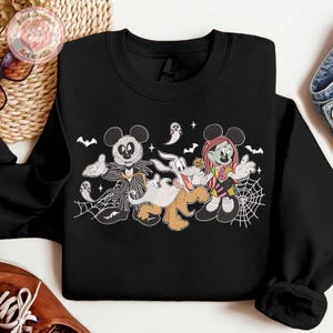 May include: Black sweatshirt featuring a Halloween-themed cartoon design. The graphic includes Mickey Mouse as Jack Skellington, Goofy as a ghost, and Minnie Mouse as a zombie. Bats, spiderwebs, and ghosts complete the spooky theme.