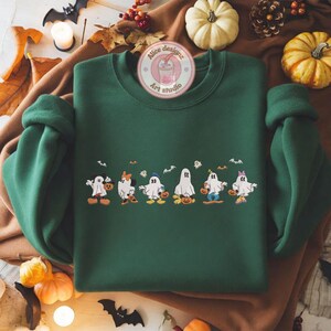 K&ouml;nnte beinhalten: Ein dunkelgr&uuml;nes Sweatshirt mit Rundhalsausschnitt und langen &Auml;rmeln, verziert mit Cartoon-Geistern in Disney-Charakterkost&uuml;men, die jeweils einen K&uuml;rbis halten. Das Bild enth&auml;lt K&uuml;rbisse, Flederm&auml;use und den Text "Alice designz Art studio".
