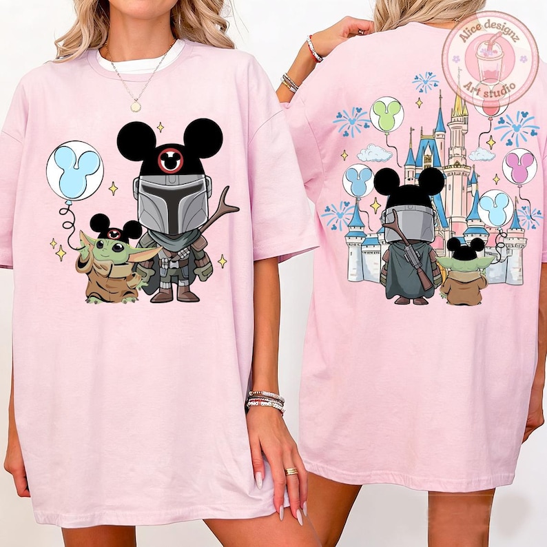 May include: Light pink t-shirt featuring a cartoon illustration of The Mandalorian and Grogu with Mickey Mouse ears. The front design includes a blue balloon. The back design shows a castle and fireworks.