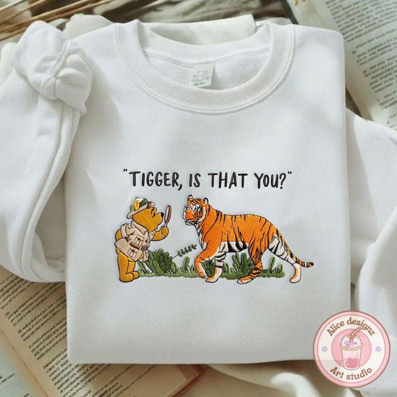 Op de afbeelding: Witte sweatshirt met een cartoon illustratie van Winnie de Poeh en Tijgertje. De tekst "Tigger, is that you?" staat boven de karakters. De sweatshirt heeft een ronde hals en lange mouwen.
