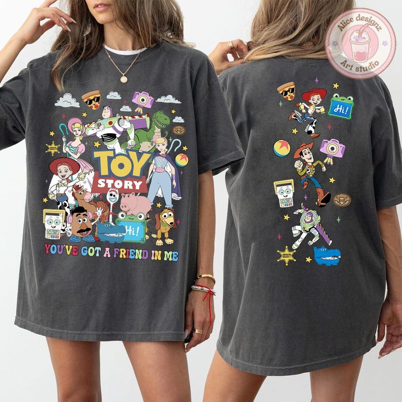 May include: A charcoal gray t-shirt featuring Toy Story character graphics on the front and back. The front displays the Toy Story logo, the text "YOU'VE GOT A FRIEND IN ME," and various characters. The back features a vertical arrangement of characters.