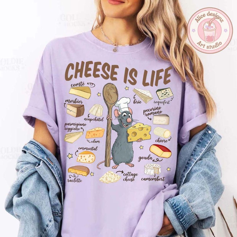Puede incluir: Camiseta lila claro con el texto "CHEESE IS LIFE" e ilustraciones de varios quesos. Un chef de dibujos animados con forma de rata sostiene una cuchara de madera y una cu&ntilde;a de queso. La camiseta tambi&eacute;n presenta el logo "Alice designz Art studio".