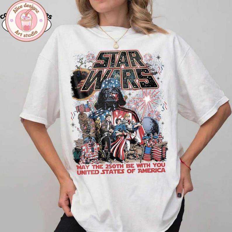 Op de afbeelding: Wit T-shirt met een Star Wars-ontwerp met Darth Vader, vuurwerk en Amerikaanse vlaggen. De tekst luidt "STAR WARS" en "MAY THE 250TH BE WITH YOU UNITED STATES OF AMERICA."