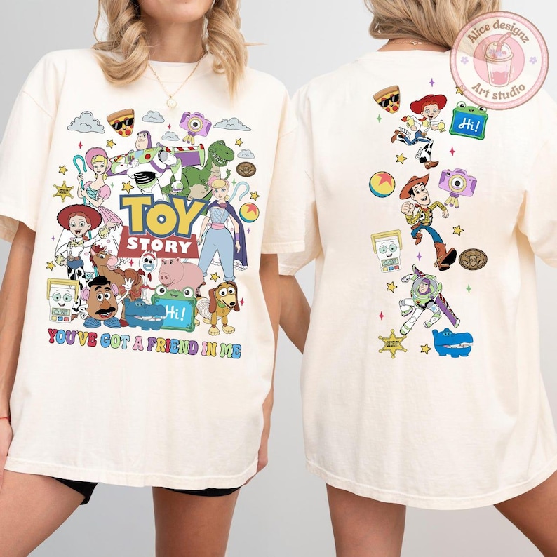 May include: An off-white t-shirt featuring Toy Story characters on the front and back. The front displays a large graphic with the text "TOY STORY" and "YOU'VE GOT A FRIEND IN ME" surrounded by various characters. The back shows a vertical arrangement of characters and icons.