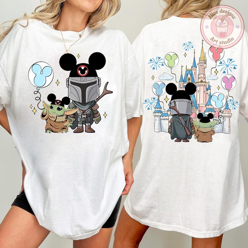 May include: White t-shirt featuring a cartoon illustration of The Mandalorian and Grogu with Mickey Mouse ears. The front design includes a blue balloon. The back design shows a castle, fireworks, and balloons.