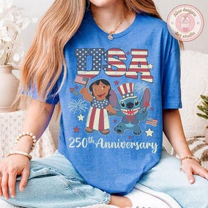 May include: A blue t-shirt featuring a graphic of Lilo and Stitch with American flag patterns, fireworks, and the text USA 250th Anniversary. The design includes a red, white, and blue color scheme with stars and stripes elements on the characters' clothing.