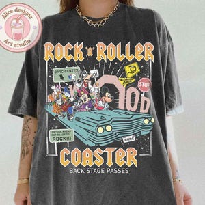 May include: A black t-shirt with a graphic print of cartoon characters riding in a vintage car. The text "Rock 'n' Roller Coaster" is printed in yellow and orange letters. The text "Back Stage Passes" is printed in white letters below the graphic.