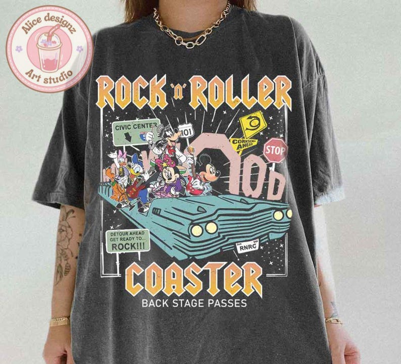 May include: A black t-shirt with a graphic print of cartoon characters riding in a vintage car. The text "Rock 'n' Roller Coaster" is printed in yellow and orange letters. The text "Back Stage Passes" is printed in white letters below the graphic.