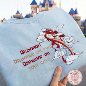 May include: Light blue sweatshirt with embroidered red dragon design and the text "Dishonor! Dishonor on you! Dishonor on your cow!" The dragon is red and tan with white clouds. The sweatshirt is held by a hand.