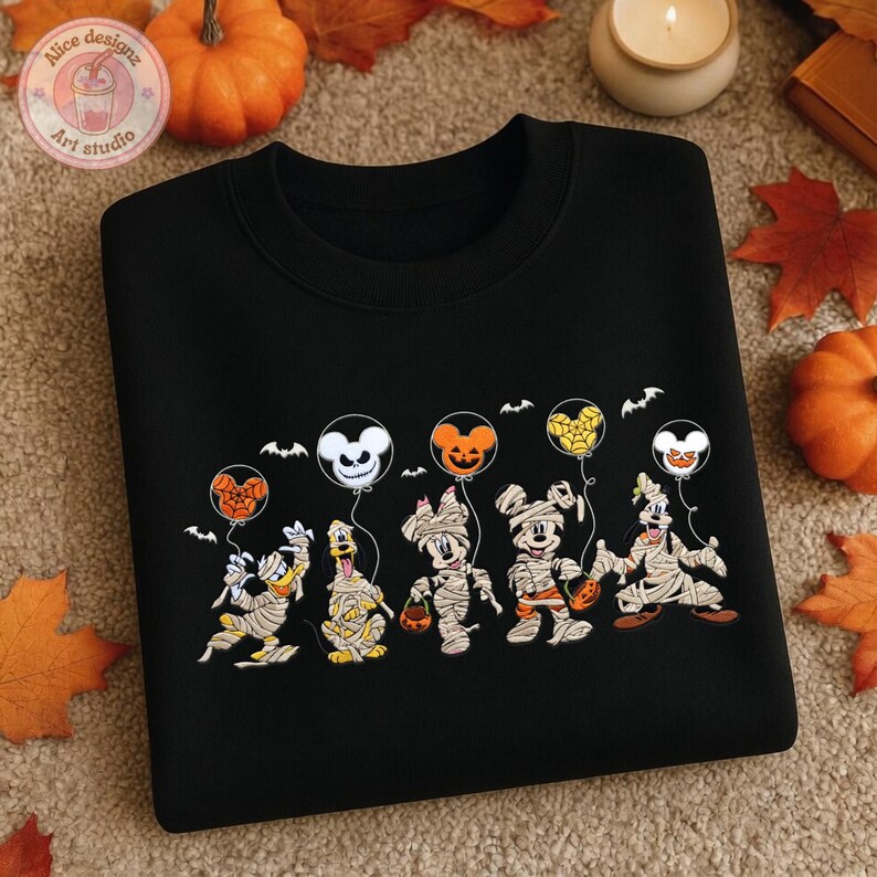 May include: Black sweatshirt featuring a Halloween-themed design. The design includes cartoon characters dressed as mummies holding balloons. The balloons have Mickey Mouse, Minnie Mouse, and other character faces. The sweatshirt has a crew neck.