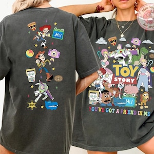 May include: A charcoal gray short-sleeve t-shirt featuring a colorful graphic print of Toy Story characters. The back displays a vertical arrangement of characters and icons, while the front shows a large group illustration with the text Toy Story and You've Got A Friend In Me.