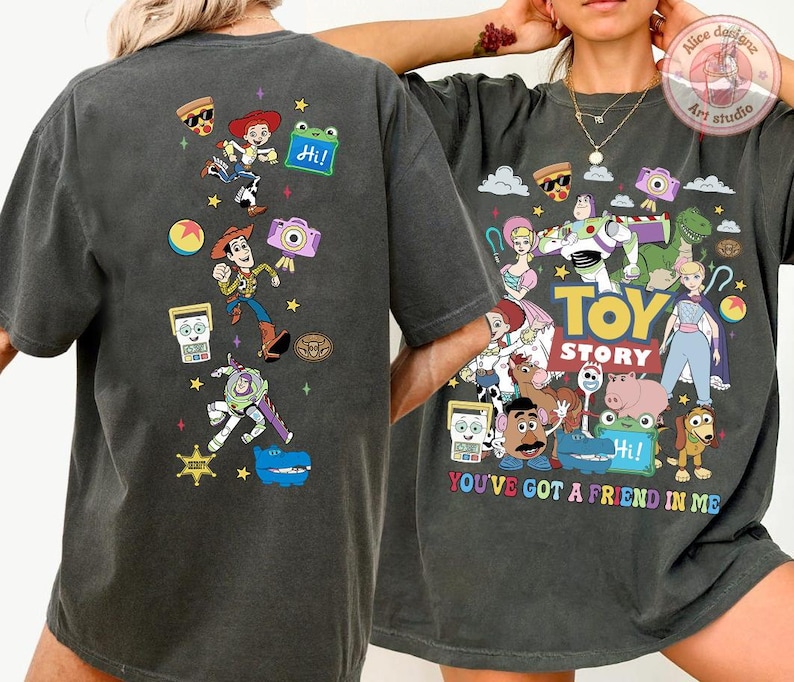 May include: A charcoal gray short-sleeve t-shirt featuring a colorful graphic print of Toy Story characters. The back displays a vertical arrangement of characters and icons, while the front shows a large group illustration with the text Toy Story and You've Got A Friend In Me.