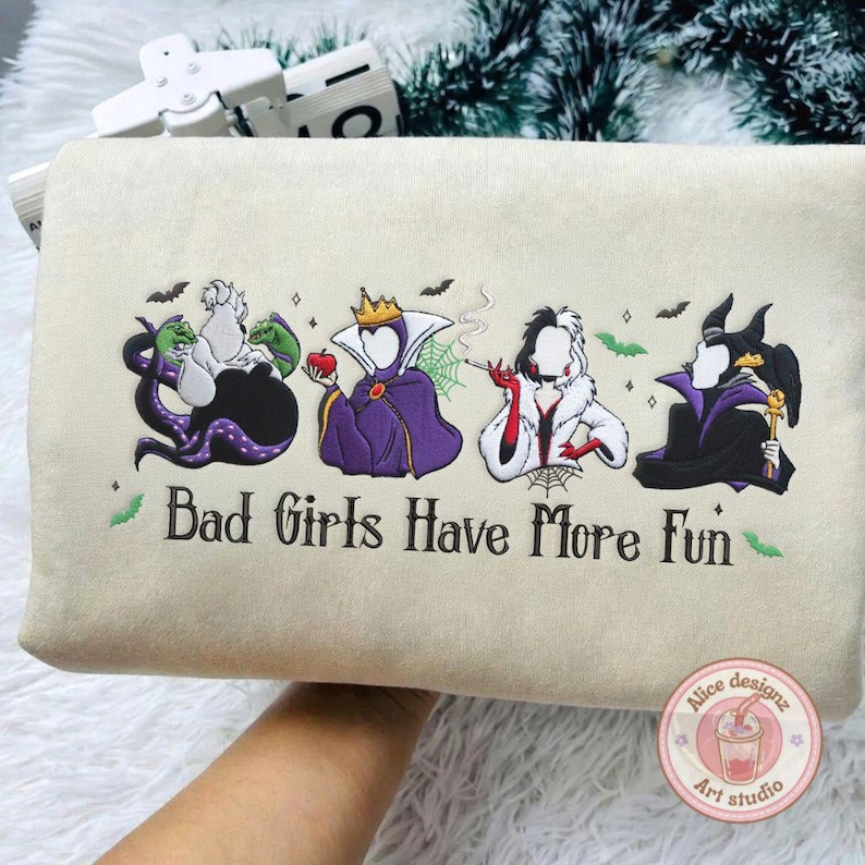 May include: Beige tote bag featuring embroidered images of four cartoon villains with the text "Bad Girls Have More Fun." The villains include Ursula, the Evil Queen, Cruella de Vil, and Maleficent, with bats and spiderwebs.