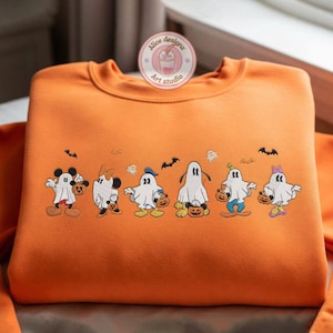K&ouml;nnte beinhalten: Orangefarbenes Sweatshirt mit einem Halloween-Motiv. Das Design zeigt Zeichentrickfiguren, die als Geister verkleidet sind und jeweils einen K&uuml;rbis halten. Flederm&auml;use und Geister sind ebenfalls auf das Sweatshirt gestickt. Der Text "Alice designz Art studio" befindet sich auf einem runden Aufkleber.