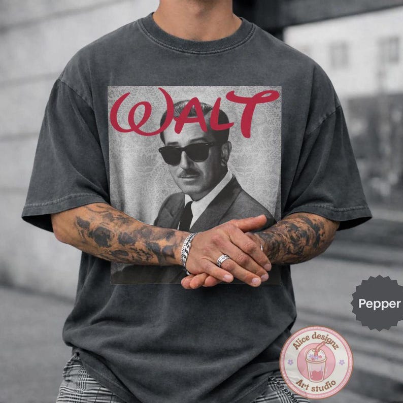 Op de afbeelding: Donkergrijze t-shirt met een zwart-wit afbeelding van een man met een zonnebril en het woord "WALT" in rode letters. Het t-shirt heeft korte mouwen en een relaxte pasvorm.
