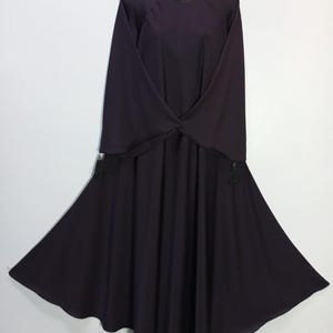 Puede incluir: Un vestido morado oscuro con mangas largas y fluidas y una falda amplia y acampanada. El vestido está colgado de un maniquí blanco y tiene un diseño simple y elegante. La tela parece ligera y adecuada para climas cálidos.