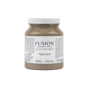 May include: A 16.9 fluid ounce bottle of Fusion Mineral Paint in the color Algonquin. The paint is a light brown color and is labeled with the Fusion logo and the name of the color.