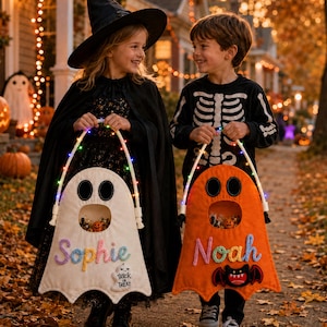 May include: Two felt ghost-shaped trick-or-treat bags with light-up handles. One white bag features the name Sophie in pastel yarn and a small ghost patch. One orange bag features the name Noah in blue yarn and a bat patch. Both have open mouths.