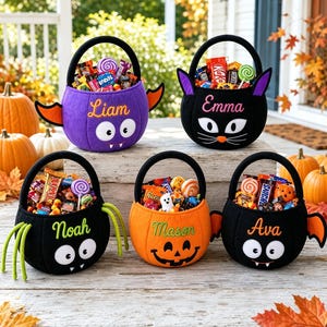 May include: Five felt Halloween candy buckets with black handles, filled with assorted candy. The buckets feature embroidered names Liam, Emma, Noah, Mason, and Ava, with designs including a purple bat, black cat, spider, pumpkin, and bat.