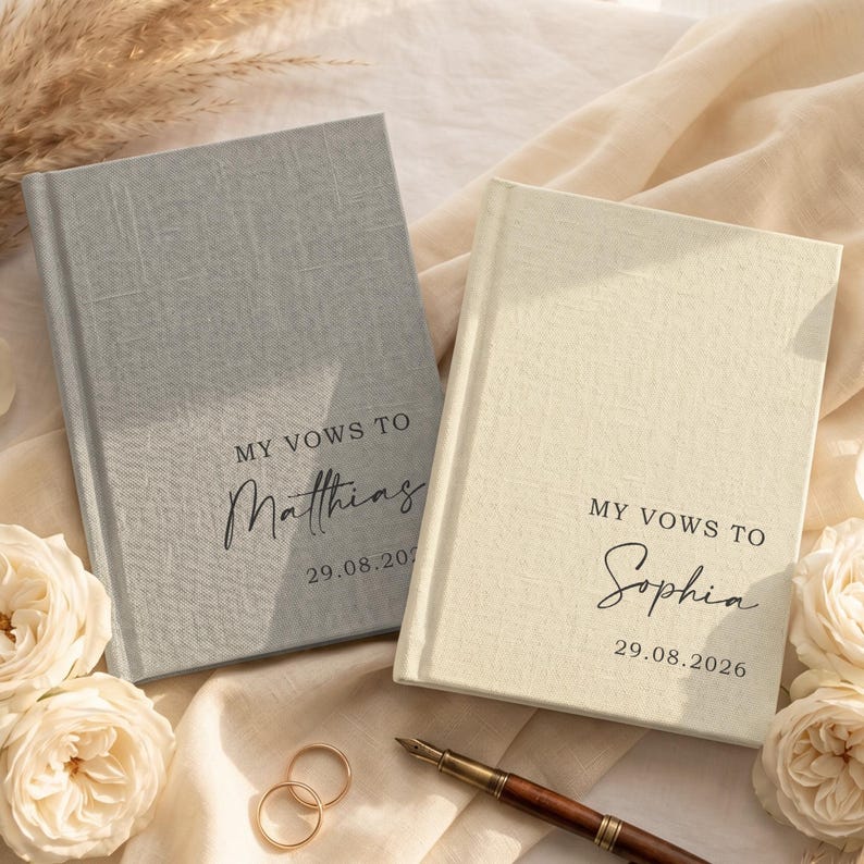 Op de afbeelding: Twee hardcover gelofteboeken met stoffen kaft, &eacute;&eacute;n in lichtgrijs en &eacute;&eacute;n in cr&egrave;me. Het grijze boek bevat de tekst "MY VOWS TO Matthias 29.08.2026" en het cr&egrave;mekleurige boek bevat de tekst "MY VOWS TO Sophia 29.08.2026" in zwarte inkt.