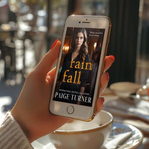 May include: A smartphone displaying the cover of the book "Rain Fall" by Paige Turner. The cover features a woman in a dark dress with the title in gold lettering. The phone has a gold-colored frame and is held in a hand with red nail polish.