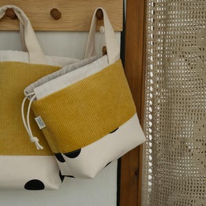 Op de afbeelding: Twee corduroy draagtassen en een zakje met trekkoord. De tassen hebben een mosterdgele corduroy bovenkant en een crèmekleurige onderkant met zwarte stippen. De draagtassen hebben crèmekleurige handvatten.
