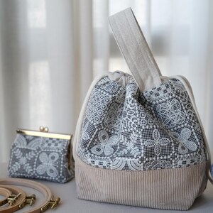 Peut inclure: Un sac bourse &agrave; cordon avec une base en velours c&ocirc;tel&eacute; beige et une partie sup&eacute;rieure en tissu noir et blanc &agrave; motif dentelle. Le sac poss&egrave;de une anse beige unique et un petit porte-monnaie assorti avec un cadre et fermoir en m&eacute;tal dor&eacute;.