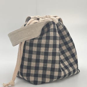 May include: A black and white gingham drawstring bag with a beige fabric handle and a beige drawstring.