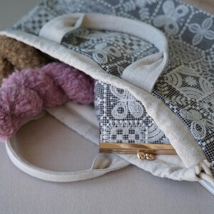 Peut inclure: Un sac fourre-tout en tissu avec un motif de dentelle g&eacute;om&eacute;trique noir et blanc et deux anses. &Agrave; l'int&eacute;rieur se trouvent deux &eacute;cheveaux de laine textur&eacute;e marron et rose, ainsi qu'un petit porte-monnaie &agrave; cadre m&eacute;tallique et fermoir dor&eacute;.