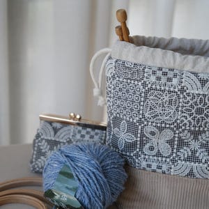 Peut inclure: Un sac &agrave; projet &agrave; cordon coulissant avec un motif &agrave; carreaux noir et blanc, une broderie florale blanche, une base en velours c&ocirc;tel&eacute; beige et une doublure beige clair. Une pochette assortie, une pelote de laine bleue et des aiguilles sont incluses.