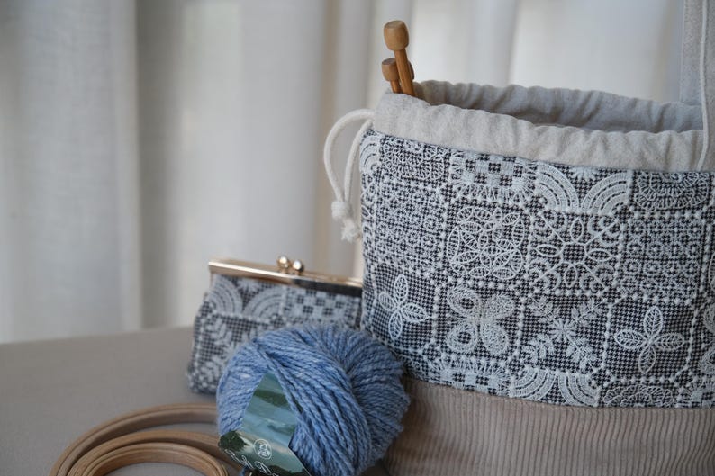 Peut inclure: Un sac &agrave; projet &agrave; cordon coulissant avec un motif &agrave; carreaux noir et blanc, une broderie florale blanche, une base en velours c&ocirc;tel&eacute; beige et une doublure beige clair. Une pochette assortie, une pelote de laine bleue et des aiguilles sont incluses.