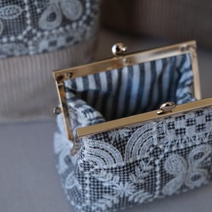 Peut inclure: Un petit porte-monnaie en tissu pied-de-poule noir et blanc avec une broderie en dentelle florale blanche. Il est dot&eacute; d'un fermoir &agrave; cliquet en m&eacute;tal dor&eacute; et d'une doublure int&eacute;rieure en tissu ray&eacute; noir et blanc.
