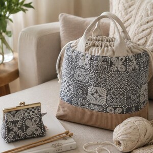 Peut inclure: Un sac seau &agrave; cordon et un porte-monnaie assorti, tous deux en tissu gris fonc&eacute; avec un motif floral blanc rappelant la dentelle et une base beige unie. Le sac poss&egrave;de deux anses et des cordons de serrage blancs pour la fermeture.