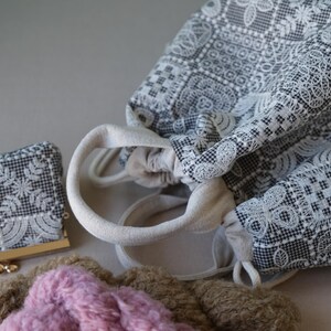 Peut inclure: Un sac &agrave; cordon et un petit porte-monnaie, tous deux dot&eacute;s d'un tissu &agrave; carreaux noir et blanc avec un motif de dentelle blanche complexe. Le sac poss&egrave;de des anses en tissu cr&egrave;me et une fermeture &agrave; cordon, accompagn&eacute; d'un objet rose textur&eacute;.