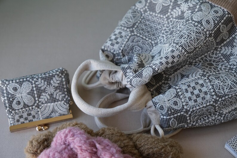 Peut inclure: Un sac &agrave; cordon et un petit porte-monnaie, tous deux dot&eacute;s d'un tissu &agrave; carreaux noir et blanc avec un motif de dentelle blanche complexe. Le sac poss&egrave;de des anses en tissu cr&egrave;me et une fermeture &agrave; cordon, accompagn&eacute; d'un objet rose textur&eacute;.