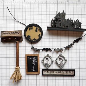 May include: A collection of Halloween-themed decorations, including a miniature haunted house, a broom with a "broom parking" sign, a circular cutout with bats and a pumpkin, and framed portraits.