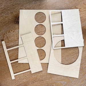 May include: Several laser-cut wooden pieces in various shapes and sizes. The pieces include rectangular and square cutouts, as well as circular and semi-circular openings. The wood has a light, natural color and appears to be unfinished.