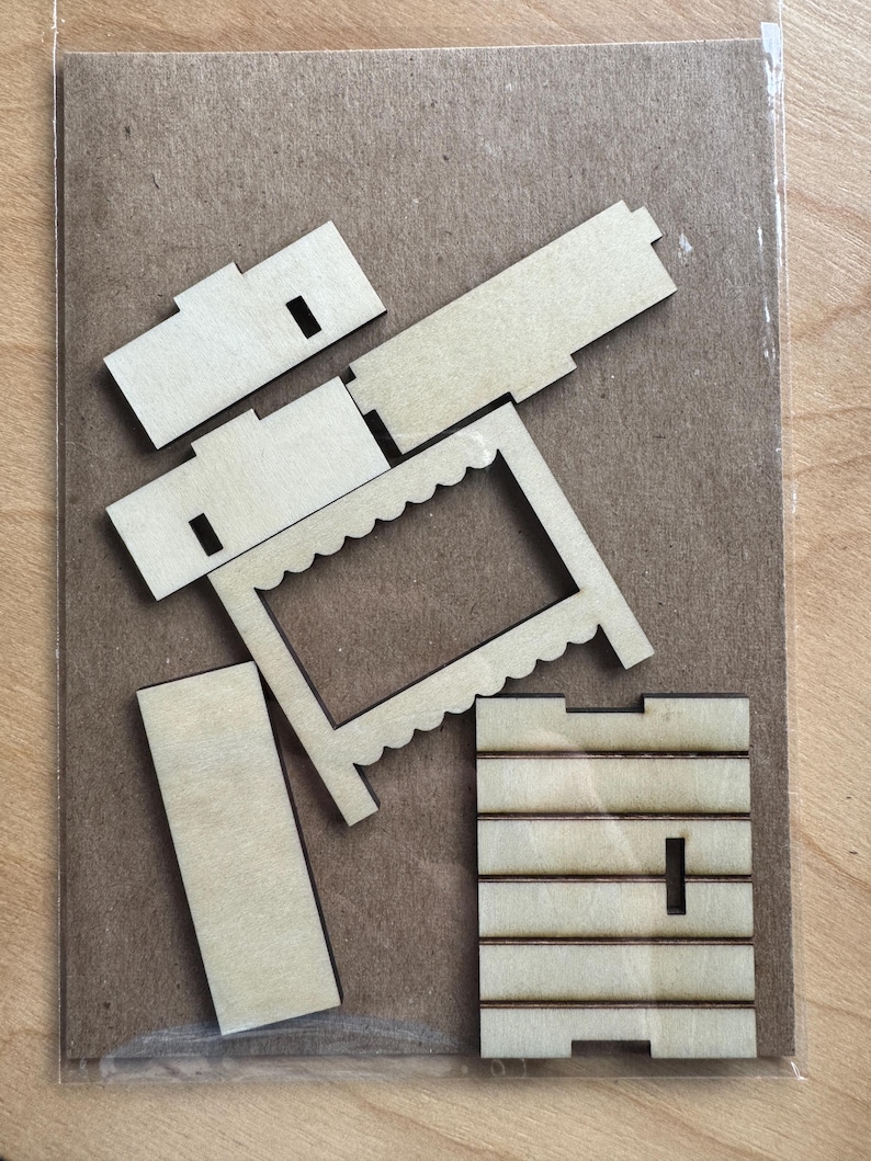 May include: A collection of unfinished wooden pieces for a craft project. The pieces include rectangular and square shapes, a scalloped frame, and parts with slots. The items are arranged on a brown cardboard backing, inside a clear plastic bag.