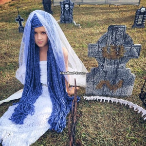 May include: A young girl dressed as a bride with long blue yarn hair, wearing a white lace dress and a white veil. She is sitting in a grassy area with a tombstone behind her that reads "RIP".
