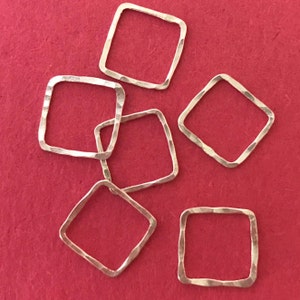 May include: Six silver-toned metal square jump rings with a hammered texture. The jump rings are on a red background.
