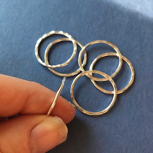 May include: Five silver hammered rings, stacked and arranged in a circle, with one ring held separately in a hand. The rings are all smooth and shiny.