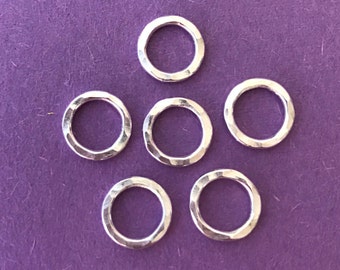 Peut inclure: Six anneaux de saut en argent avec une texture martelée. Les anneaux sont disposés en forme de triangle sur un fond violet.